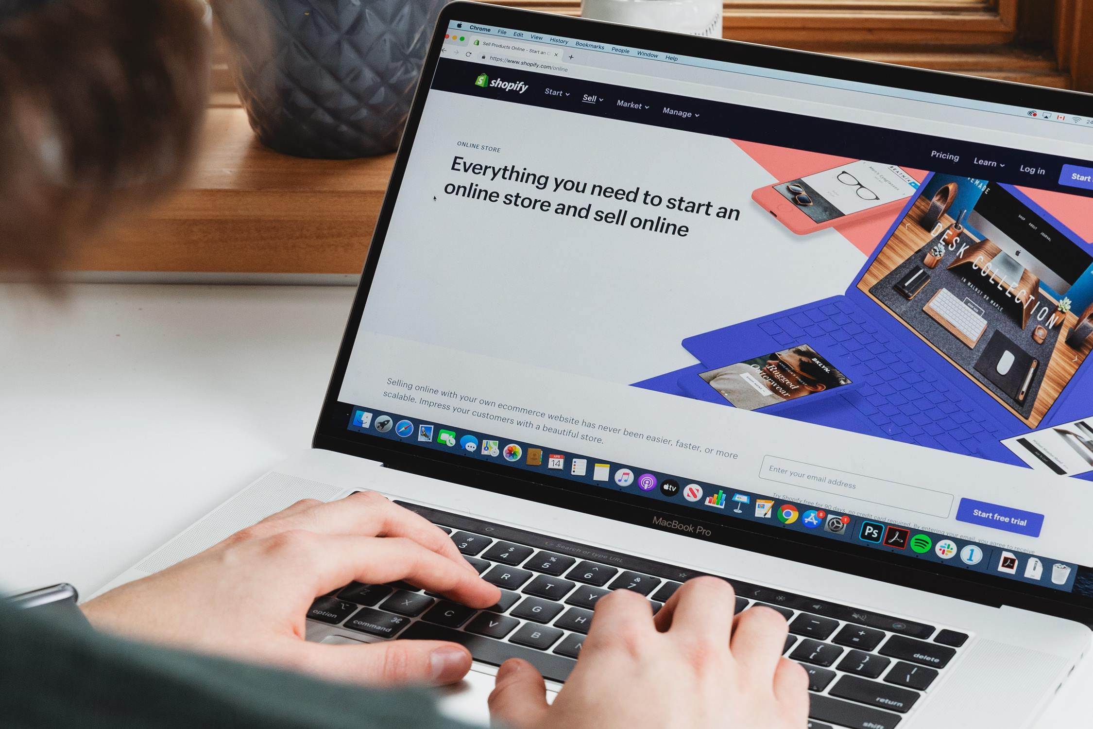 Hands resting on laptop keyboards with Shopify's homepage displayed on the screen.