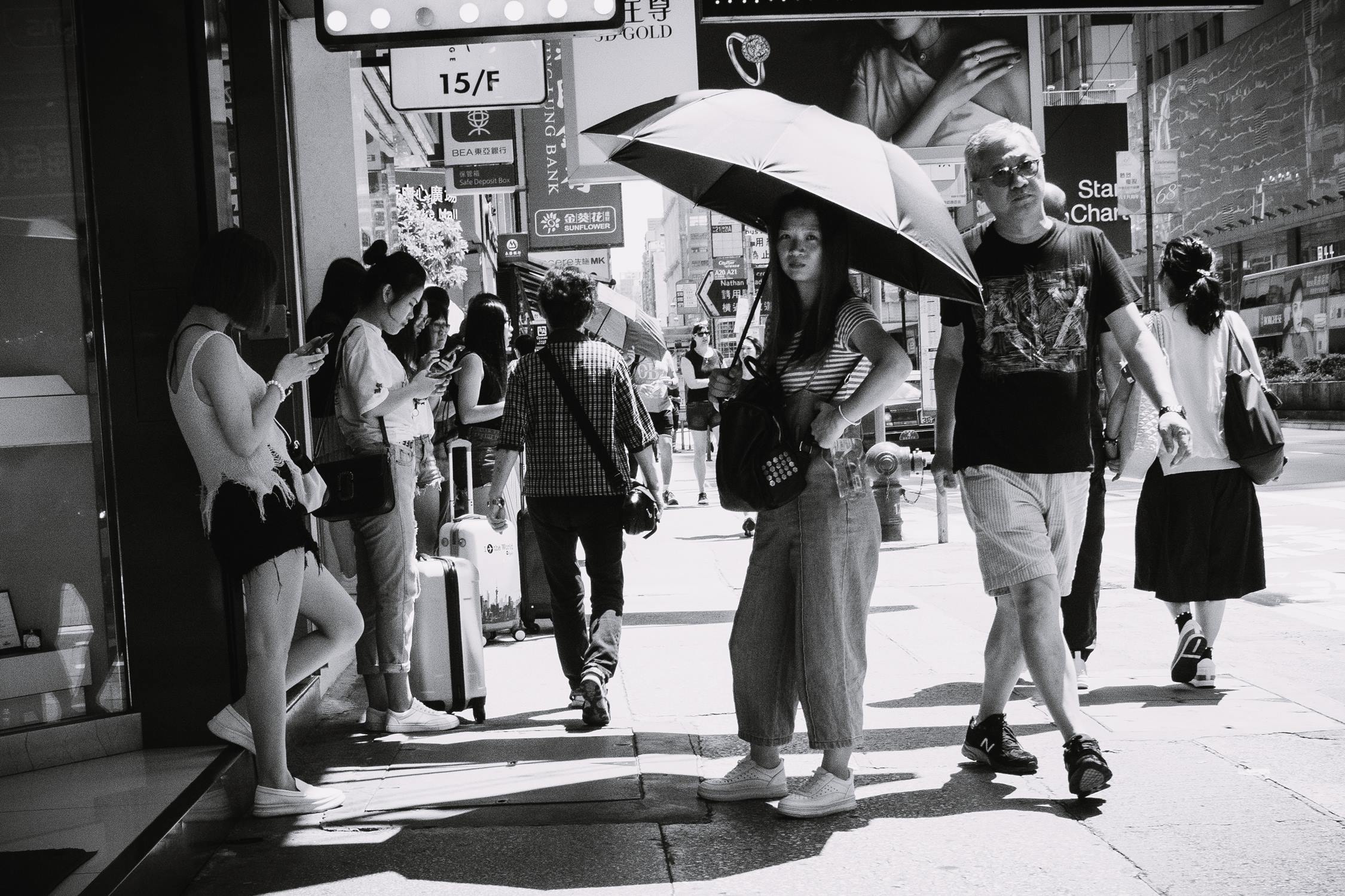 A black and white city sidewalk street filled with people walking and standing.