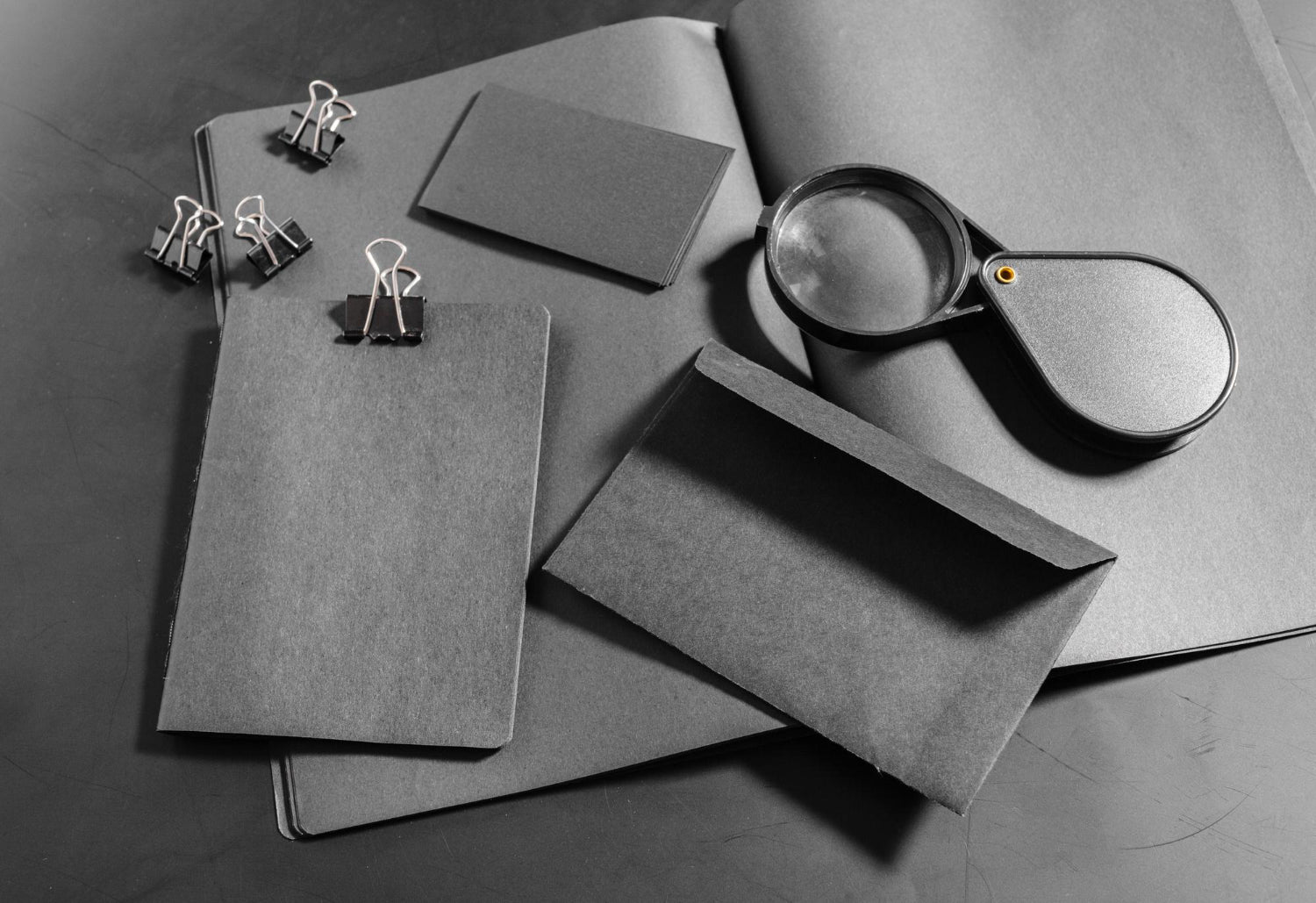 Black paper and notebook with paper clips and magnifying glass