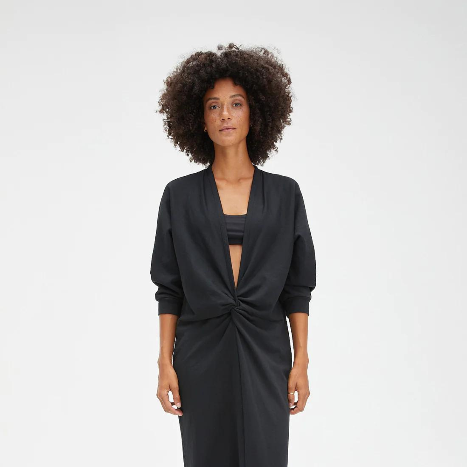 Woman with natural afro hair wearing a low-neck, black ruched dress.