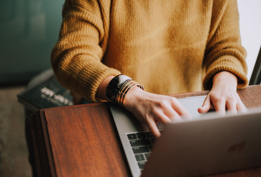 A person's torso wearing a yellow sweater typing on a laptop.
