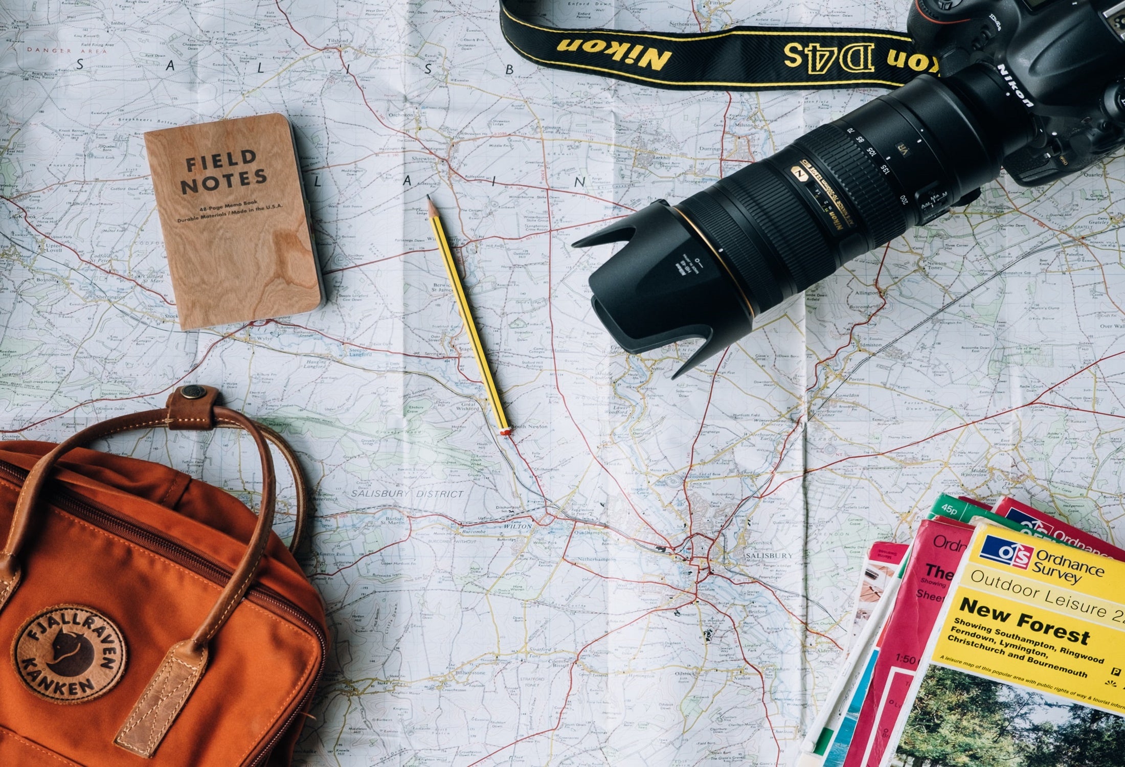 A flat lay of a bag, camera, notebook, and various guides across an open map.