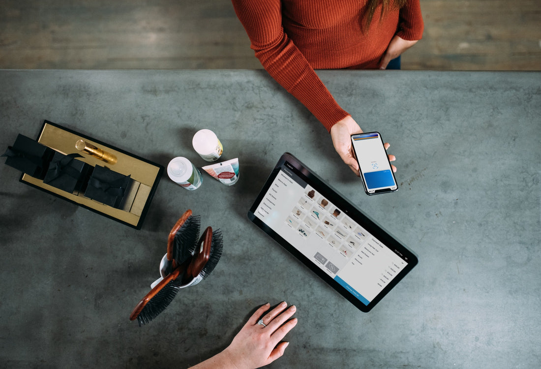 A flat lay of peoples hands, a mobile phone, tablet, and hair grooming products.