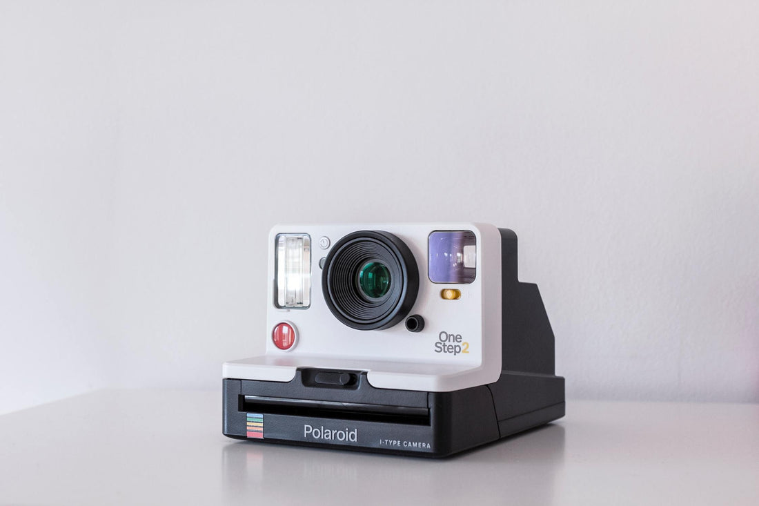 A polaroid camera on a white table with a white background.