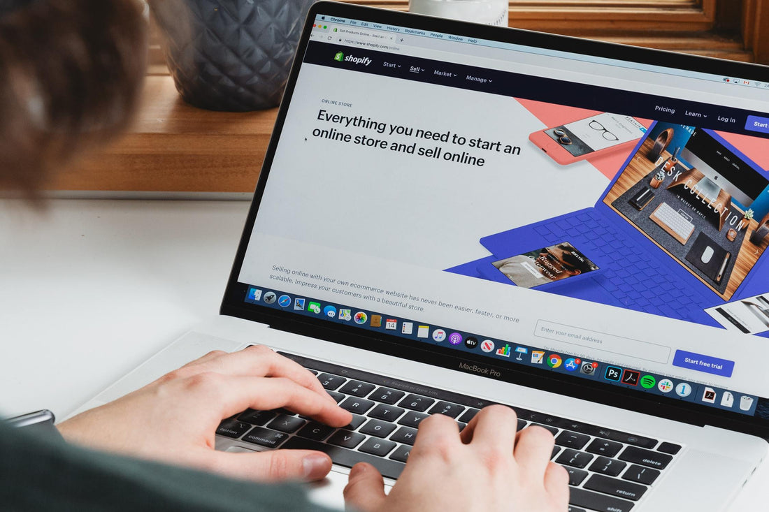 Hands resting on laptop keyboards with Shopify's homepage displayed on the screen.