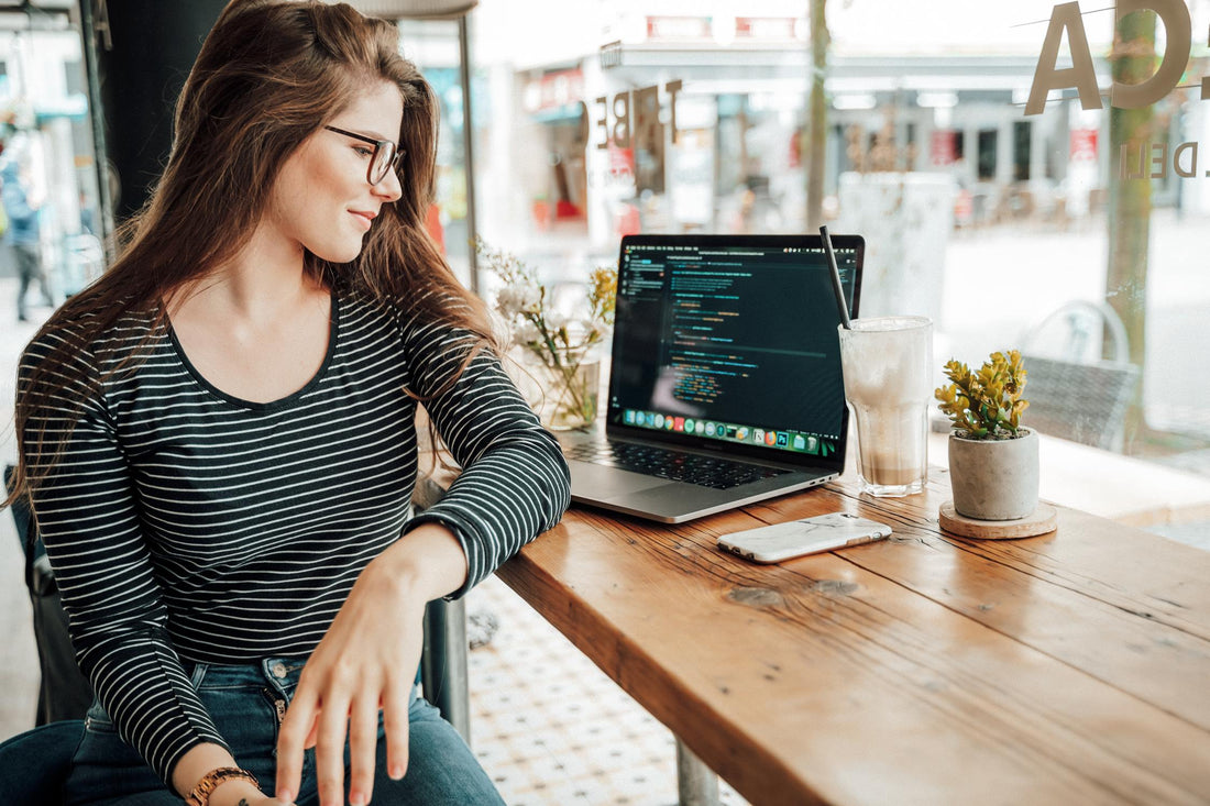 A woman sitting by a wooden table looking at her laptop.