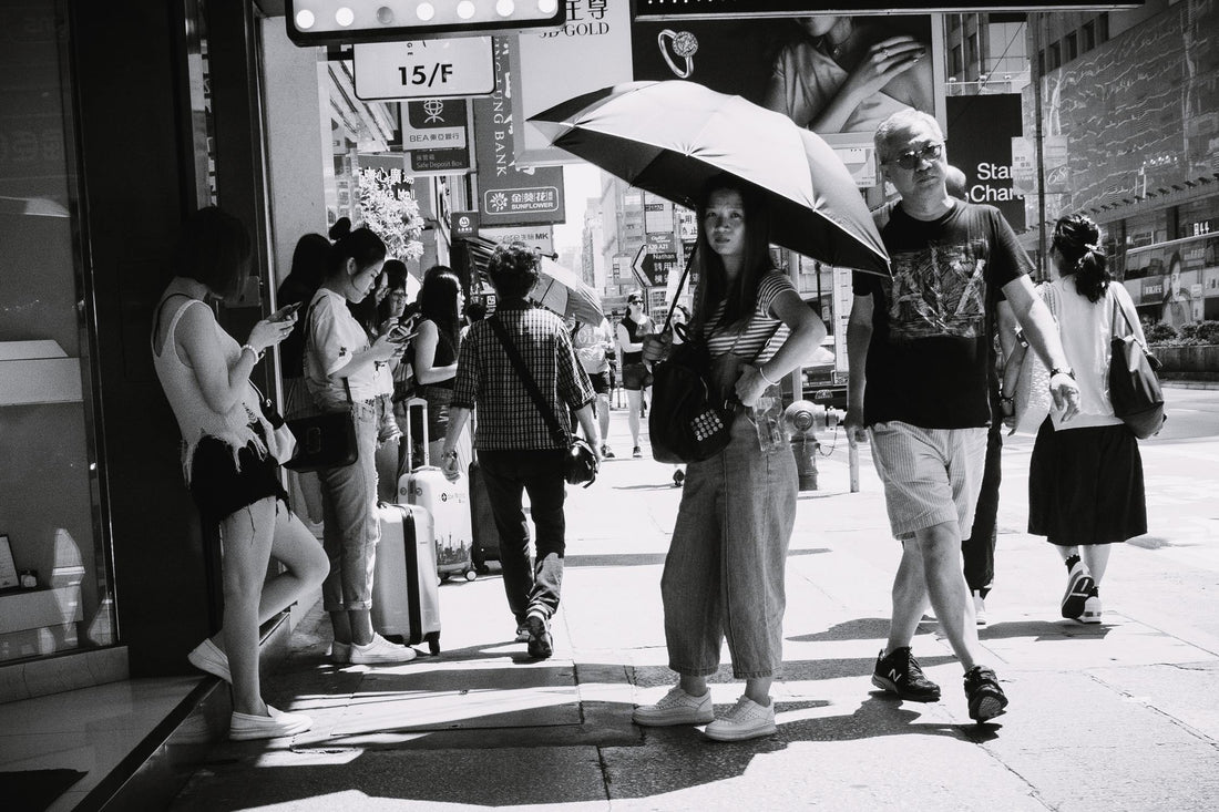 A black and white city sidewalk street filled with people walking and standing.