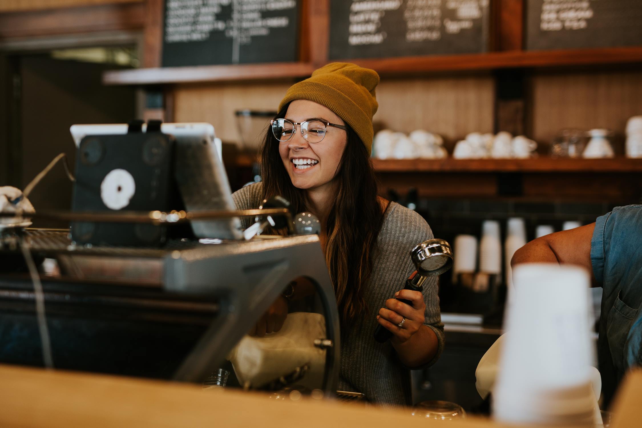 A smiling lady barista behind the bar with a coffee machine.