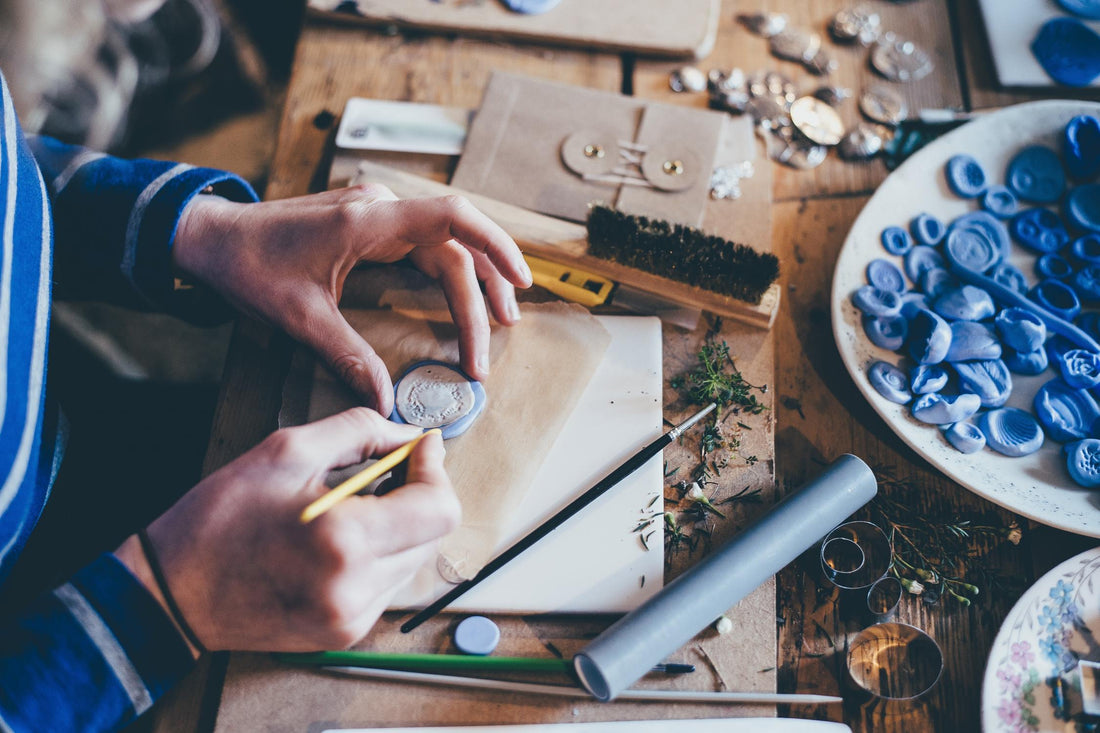 Two hands making crafts over a crowded crafts table and desk.