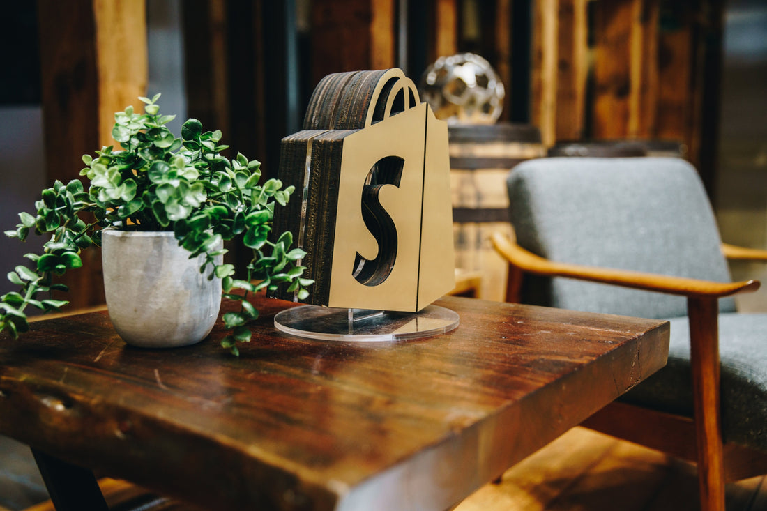 A small dining table with a potted plant and shopping bag with a Shopify logo.