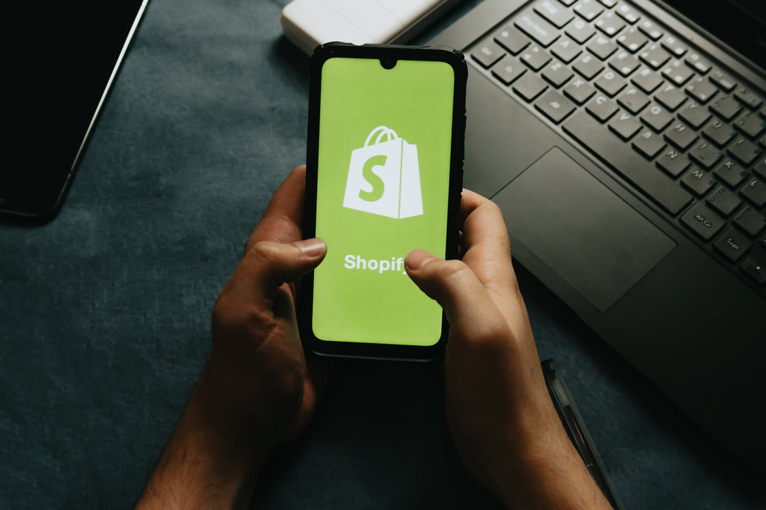 A person's hands holding a smartphone, displaying the Shopify logo on the screen.