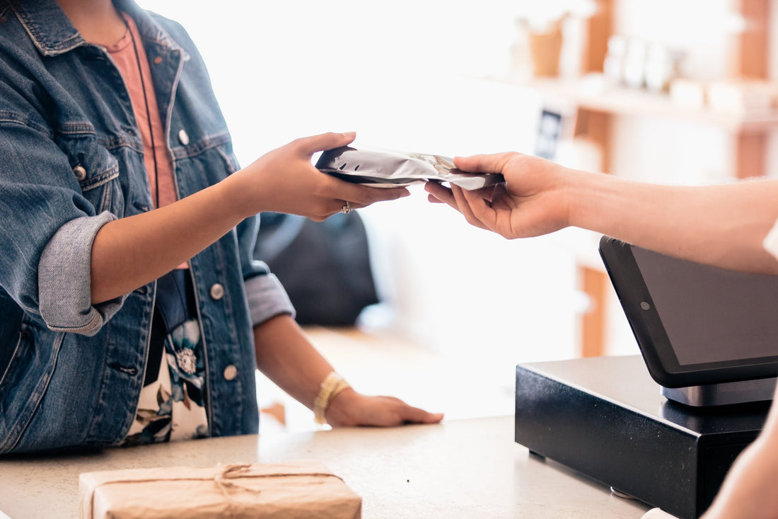 Two hands passing a newly purchased item across a shop checkout table.