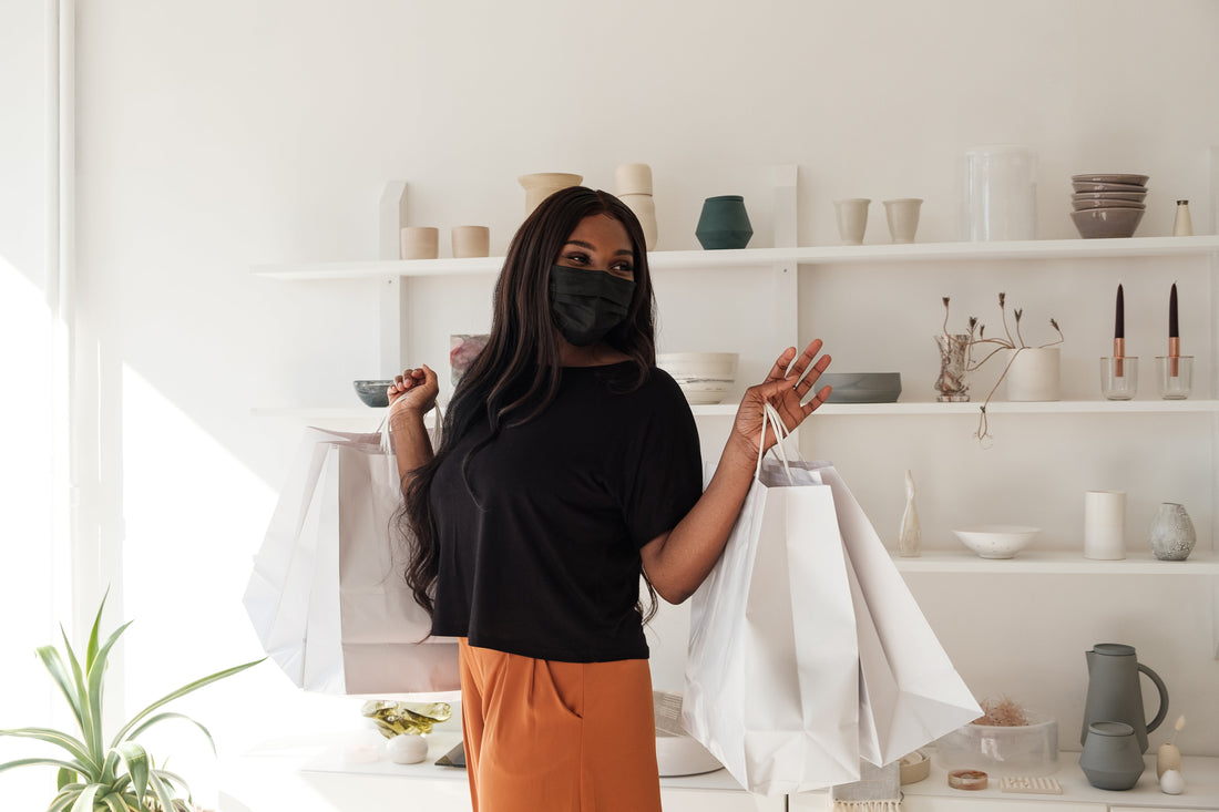 A woman wearing a mask holding plain white shopping bags in a ceramic store.
